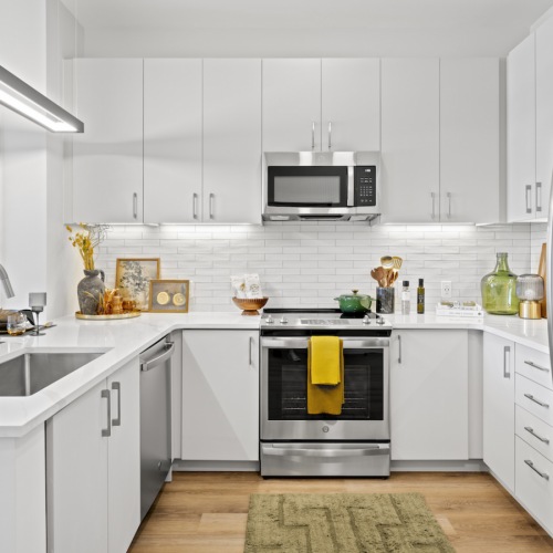 Model apartment kitchen at The Brookliner in Boston featuring a kitchen island with quartz countertops, white cabinets, and stainless steel appliances.